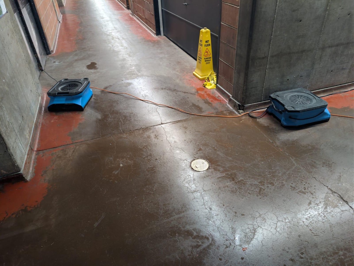 Air movers drying a wet parking garage corridor behind a wet floor sign