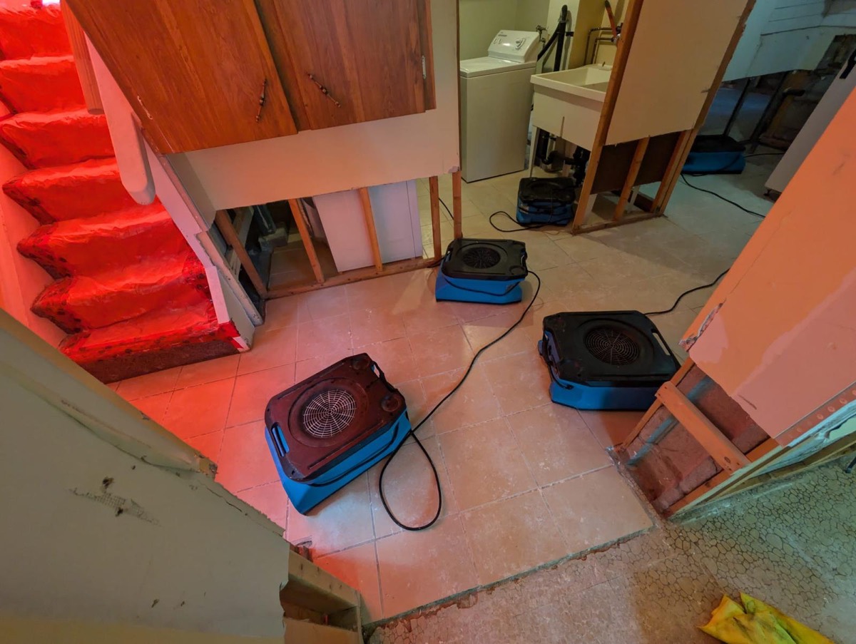 Air movers drying a basement by the patio door after a flood cut