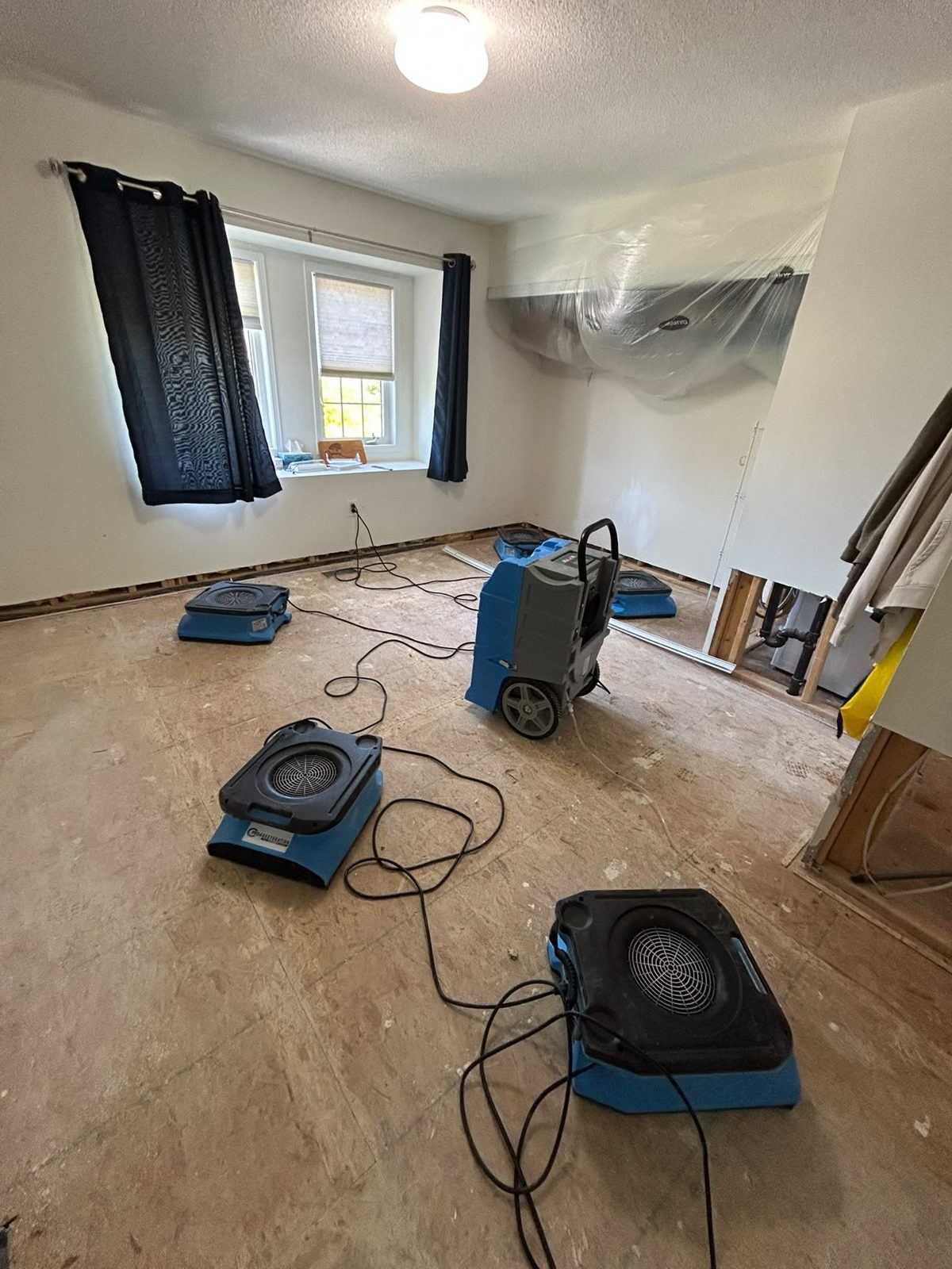 Air movers and a dehumidifier drying a bedroom subfloor after the carpet was removed