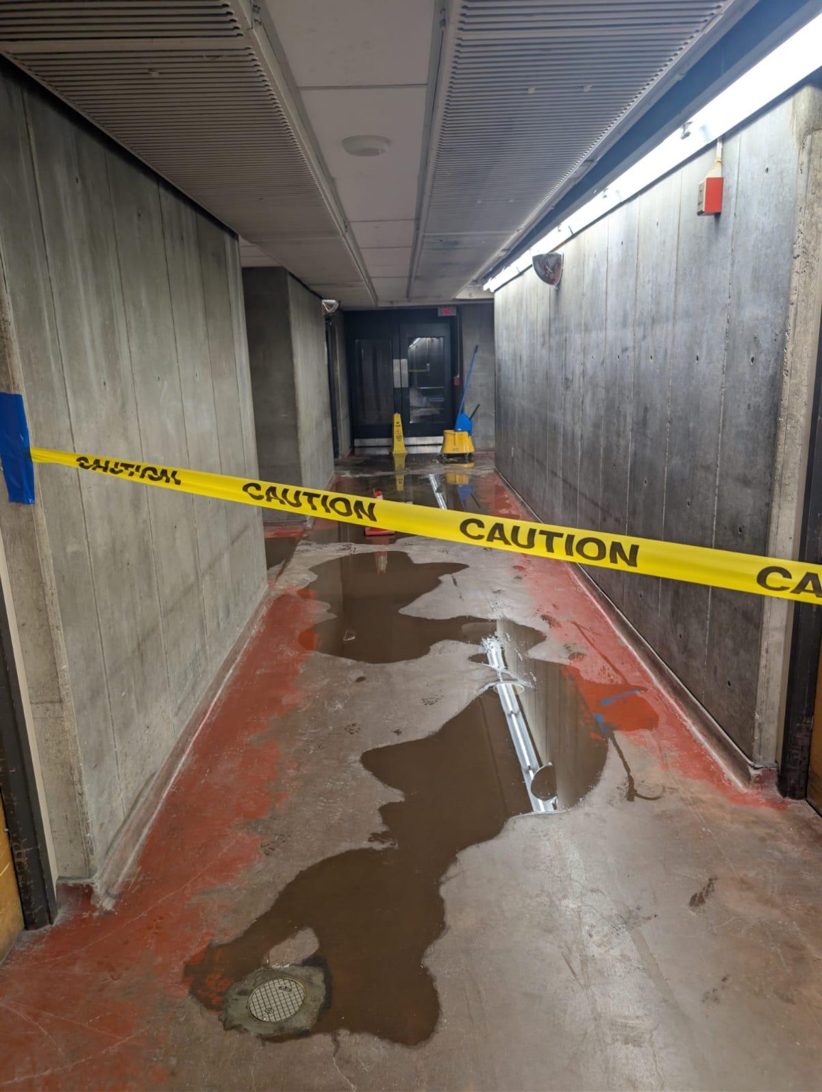 Caution tape across a commercial corridor with standing water on the floor