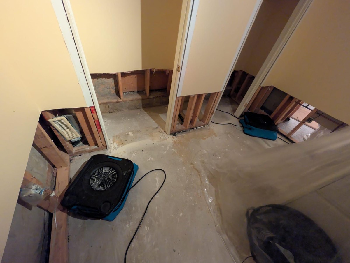 Air movers drying a hallway with the drywall cut out and the framing exposed