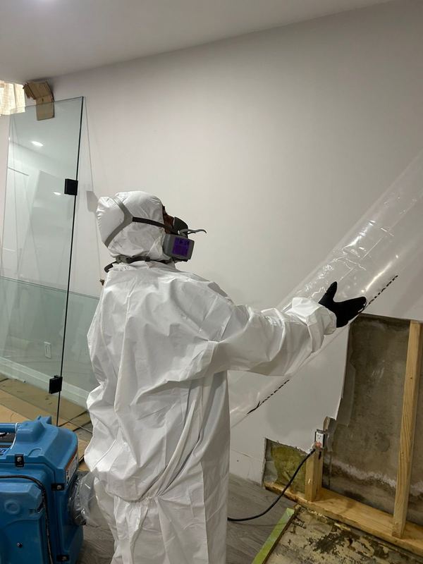 Safesite technician in a protective suit sealing a room with containment for mold removal